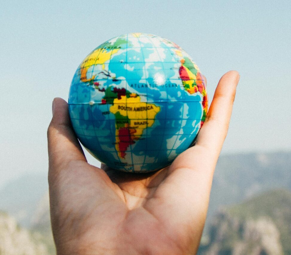 Person Holding World Globe Facing Mountain